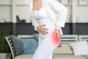 Mulher segurando o quadril esquerdo iluminado em vermelho para indicar dor, simbolizando os sintomas de artrose de quadril