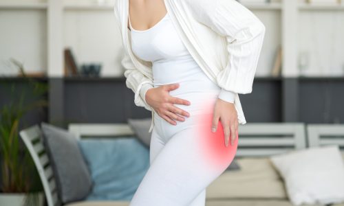 Mulher segurando o quadril esquerdo iluminado em vermelho para indicar dor, simbolizando os sintomas de artrose de quadril